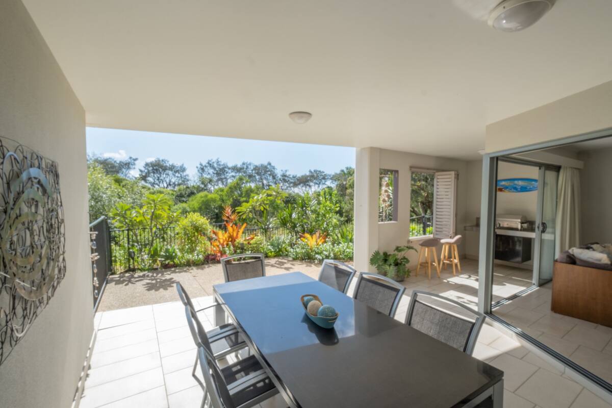 A modern dining area with a large table and chairs, a glass partition, and a view of a lush garden.