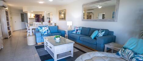 A living room with a blue sofa, a white sofa, a coffee table, and a large mirror on the wall.