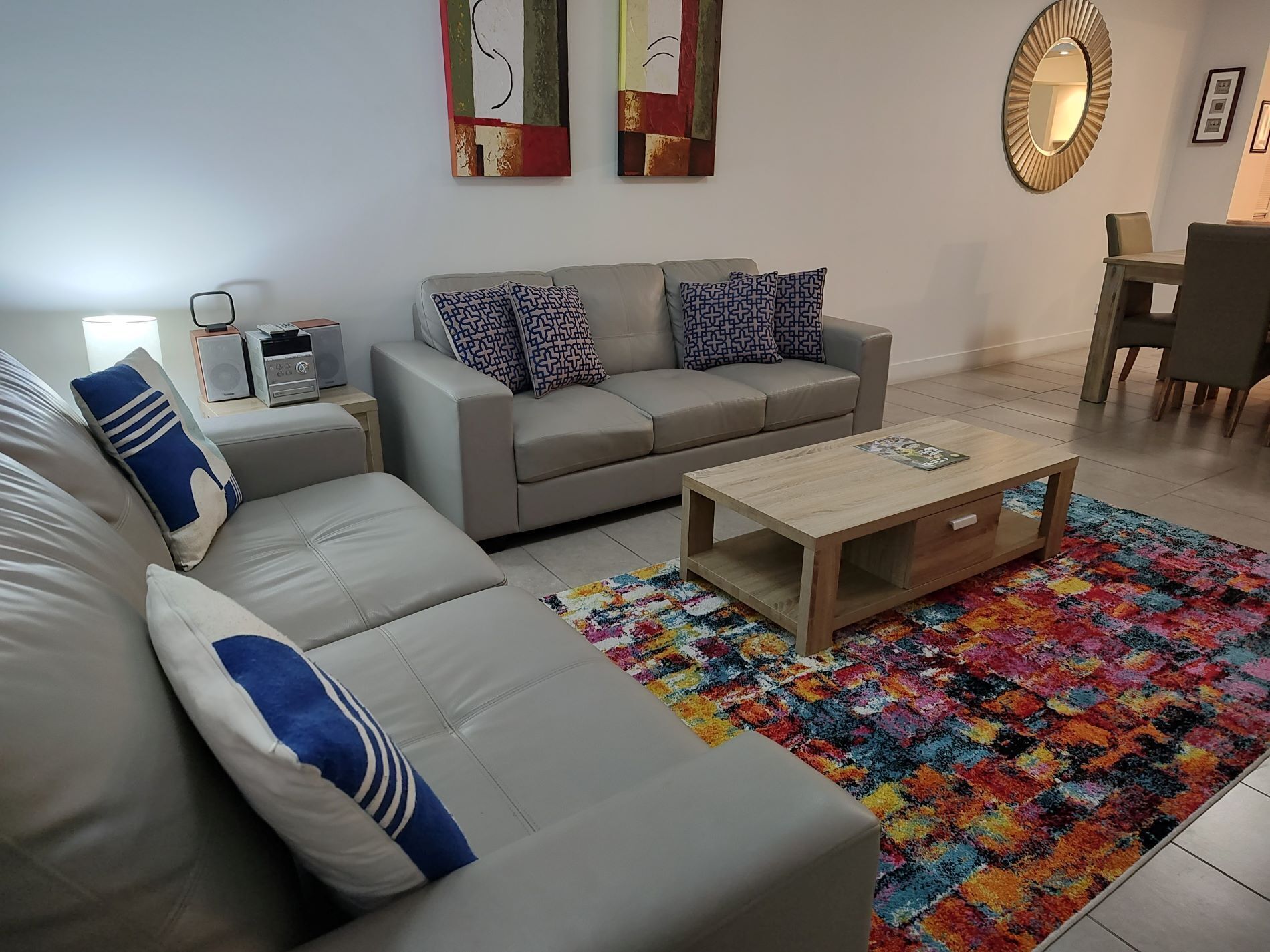 Een moderne woonkamer met een grijze bank, een houten salontafel en een kleurrijk vloerkleed.