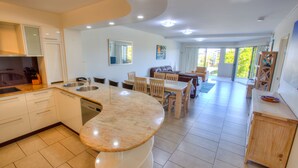 Una cocina moderna con una isla central, un comedor con mobiliario de madera y vistas al exterior a través de amplios ventanales.