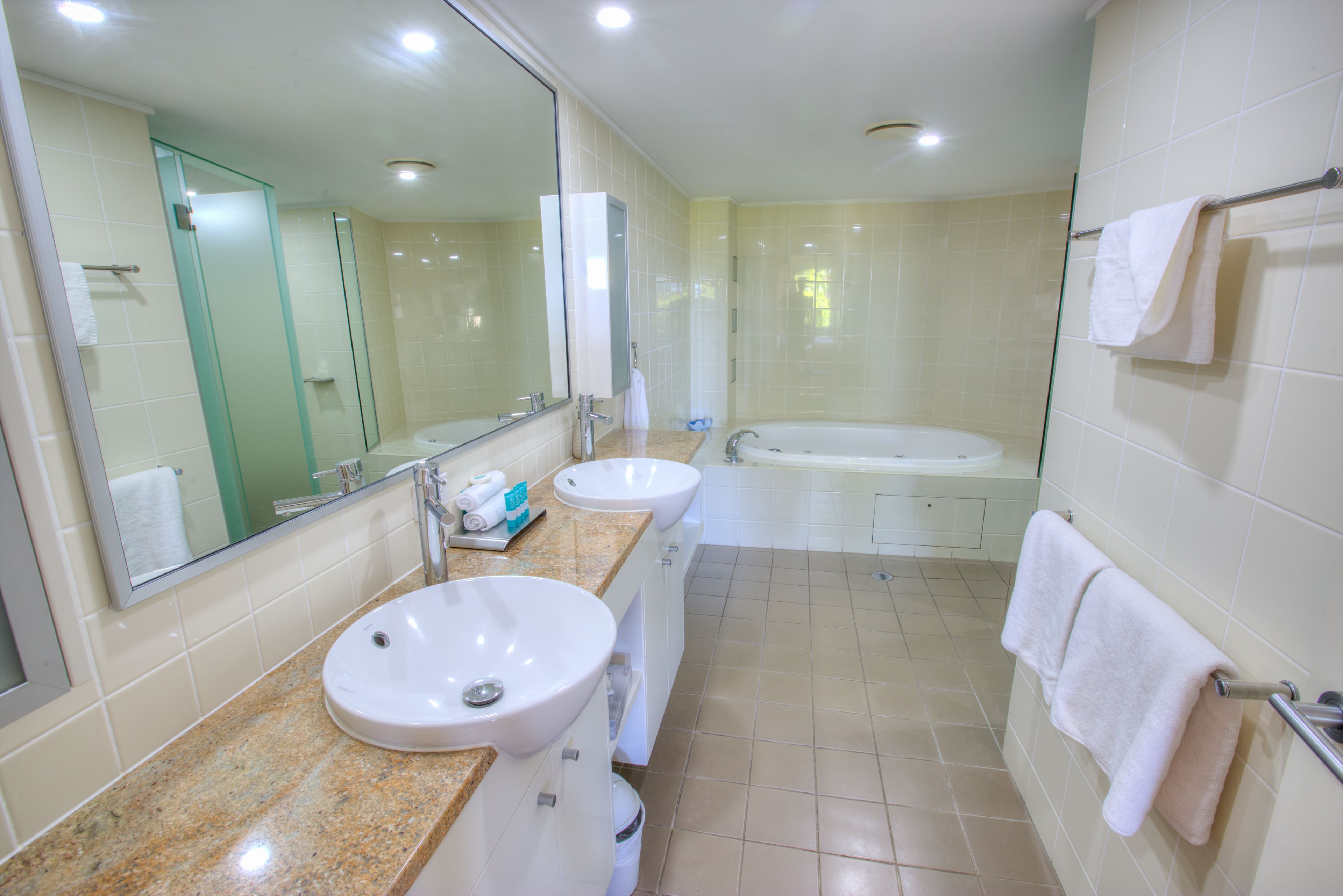 A modern bathroom with two sinks, a large mirror, a bathtub, and a glass shower enclosure.