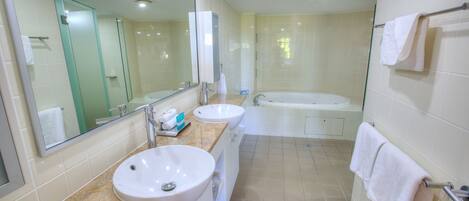 A modern bathroom with two sinks, a large mirror, a bathtub, and a glass shower enclosure.