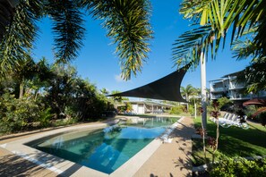 A swimming pool surrounded by palm trees and a building with a sloped roof. - Pavillions on 1770 (Agnes Water)