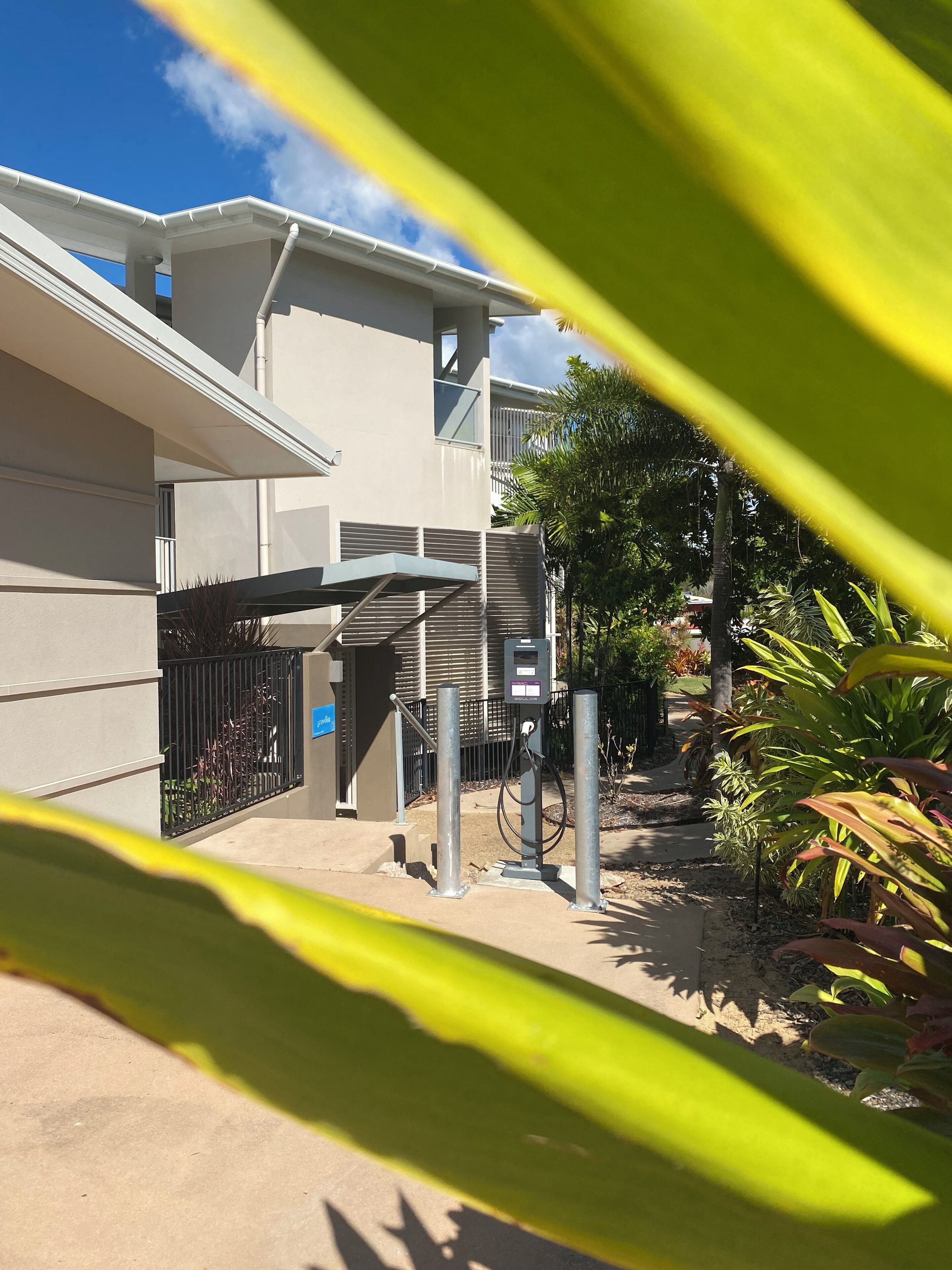 A modern building with a covered outdoor area, a utility box, and surrounding greenery.