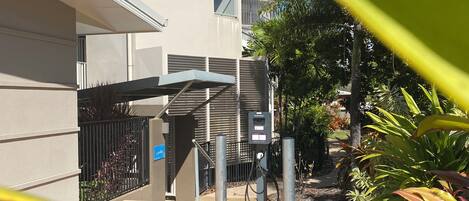 A modern building with a covered outdoor area, a utility box, and surrounding greenery.
