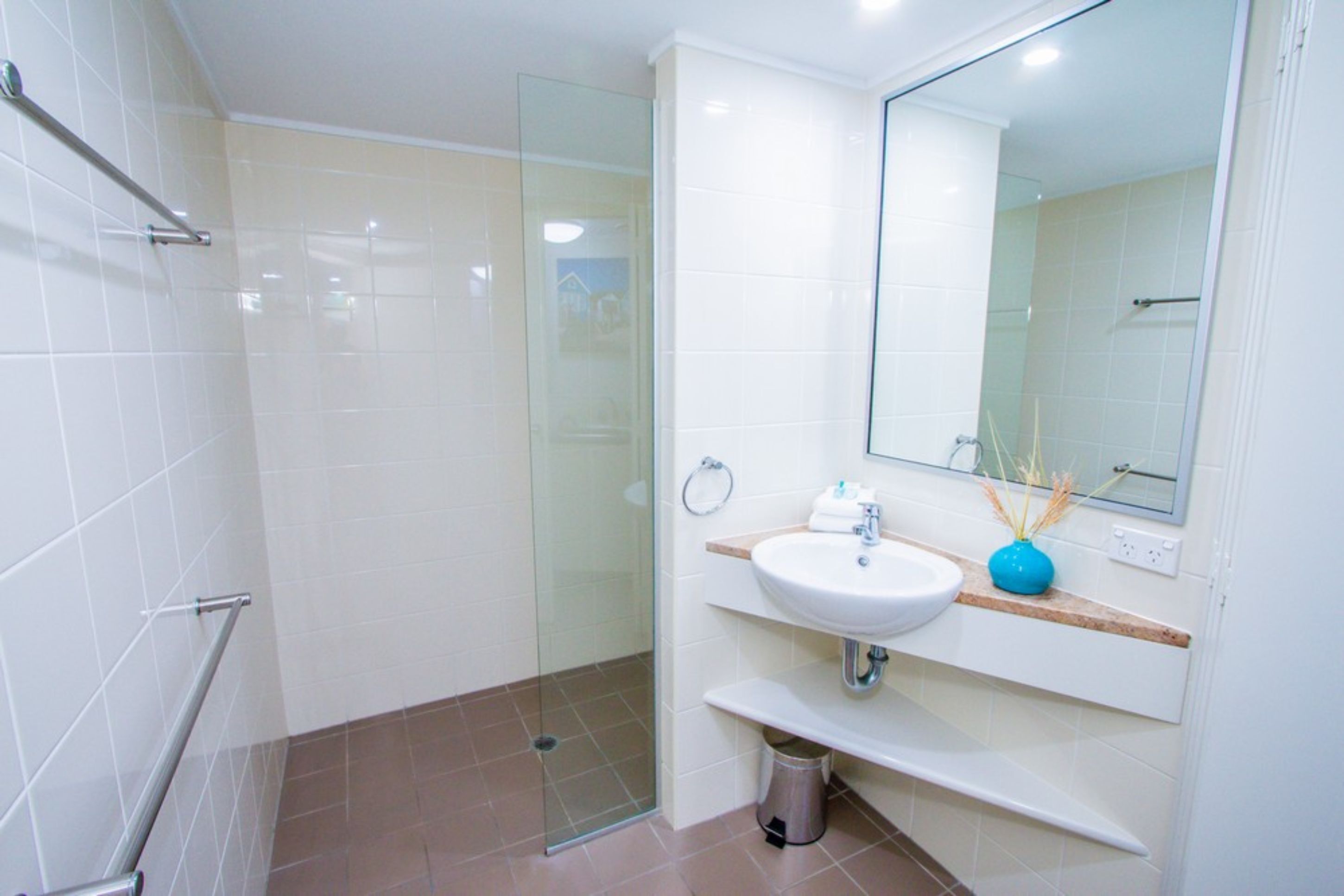 A modern bathroom with a glass shower enclosure, a white sink, and a mirror above it.