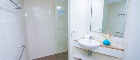 Un baño moderno con cabina de ducha de vidrio, un lavabo blanco y un espejo encima.