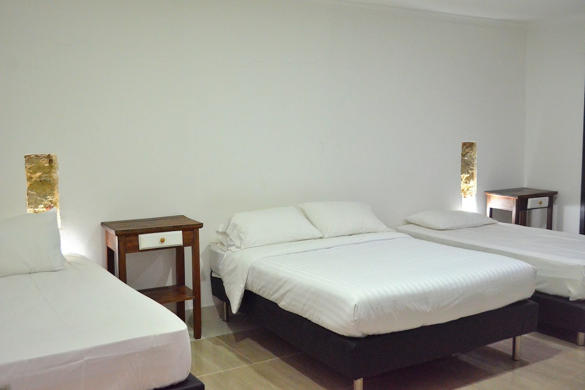 A hotel room with two single beds, a wooden nightstand with a drawer, and a small table with a lamp.
