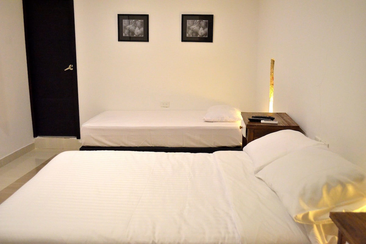 A hotel room with two beds, a nightstand with a lamp, and two framed pictures on the wall.