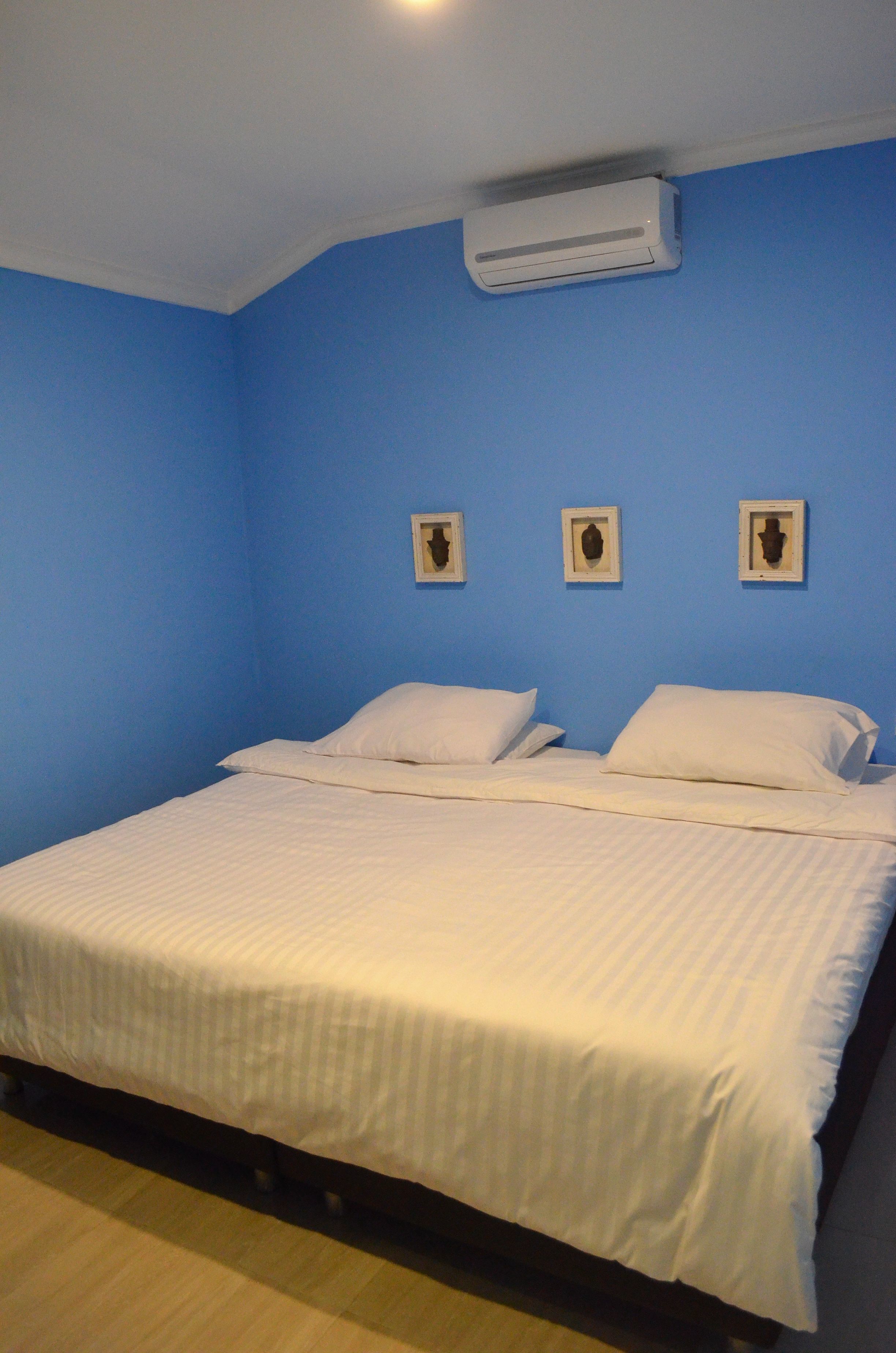 Une chambre avec un lit simple, des murs bleus et un appareil de climatisation installé au-dessus du lit.