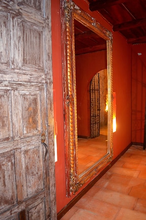 Une porte en bois avec un grand miroir qui reflète une pièce dont le mur est rouge et le sol est recouvert de carreaux.