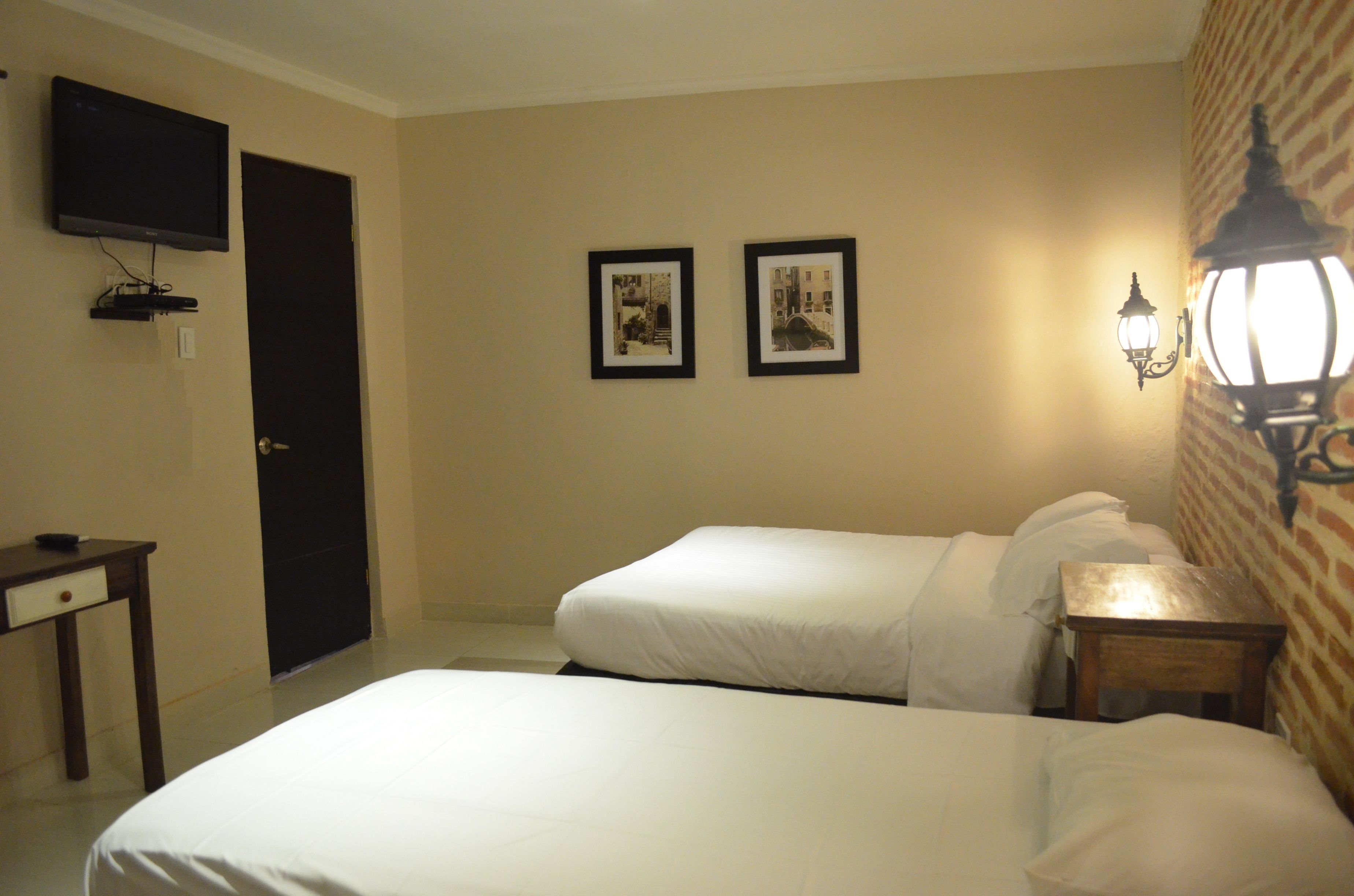 A hotel room with two beds, a TV, framed pictures on the wall, and a nightstand with a lamp.