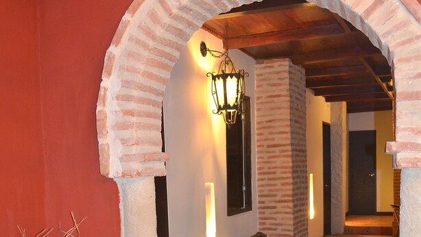 A hallway with a brick archway, a bench, and a decorative vase. - Hotel Galería la Trinidad (Cartagena)
