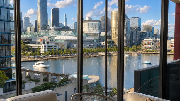 A modern hotel room with a large window overlooking a city skyline, a waterfront, and a bridge. - Harbour Escape Apartments (Docklands)