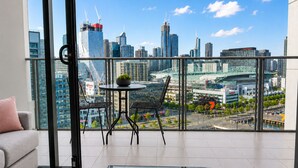 A modern room with a glass table, a sofa, and a balcony with a city view. - Harbour Escape Apartments (Docklands)