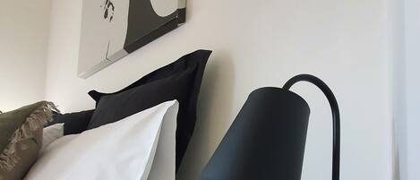 A neatly made bed with white and black bedding, a modern black desk lamp, a digital clock, and a heart-shaped object on a marble table.