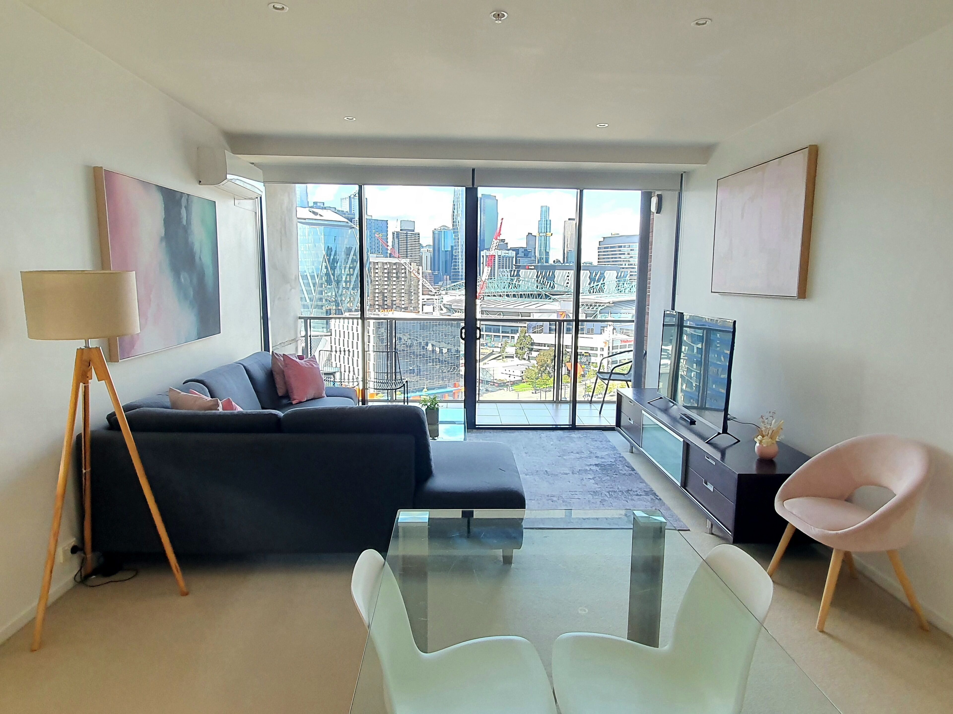 A modern living room with a large window, a sofa, a glass table, and a TV.