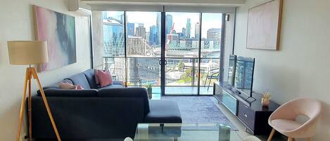 A modern living room with a large window, a sofa, a glass table, and a TV.