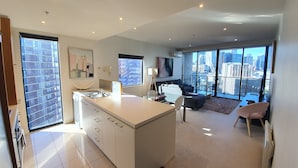 A modern apartment with a kitchen, dining area, and living room, featuring large windows and a city view. - Harbour Escape Apartments (Docklands)