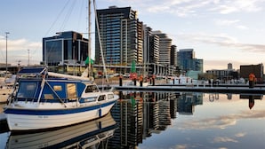 A marina with a sailboat docked, surrounded by modern buildings and a calm water surface reflecting the structures. - Harbour Escape Apartments (Docklands)