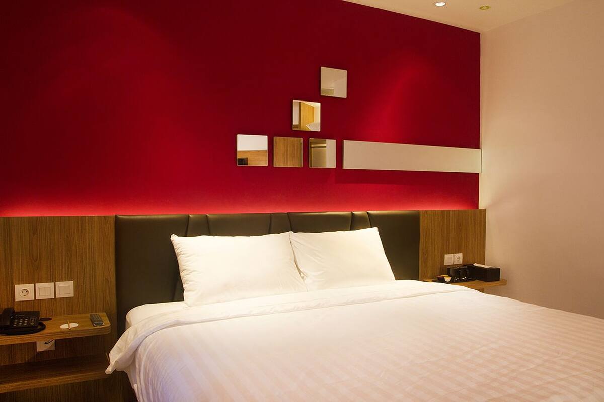 Una habitación de hotel moderna con una cama grande, un cabecero de madera y una pared de acento roja con espejos.