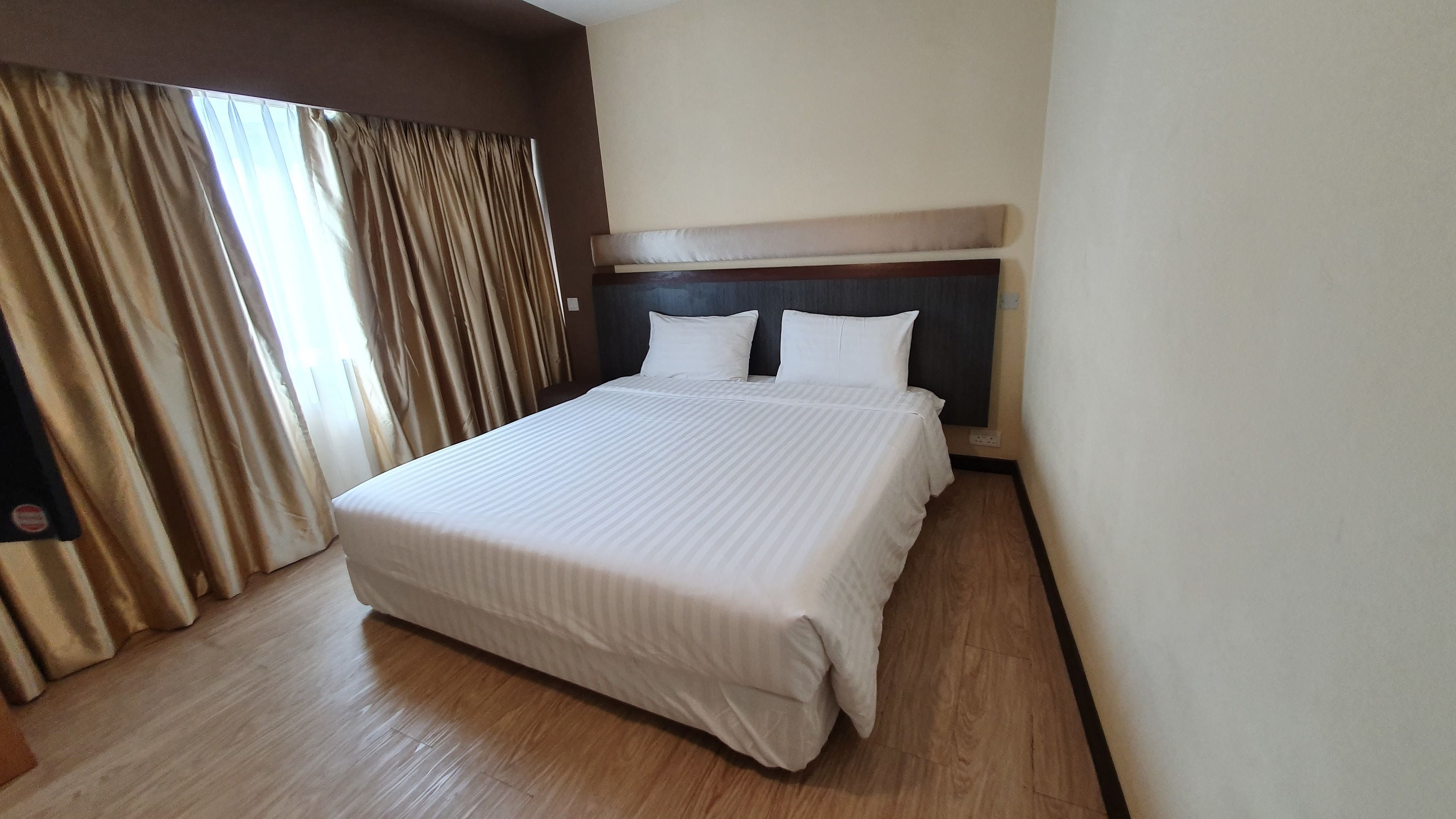 Camera d'albergo con un letto grande, pavimento in legno, una testiera e tende color beige.