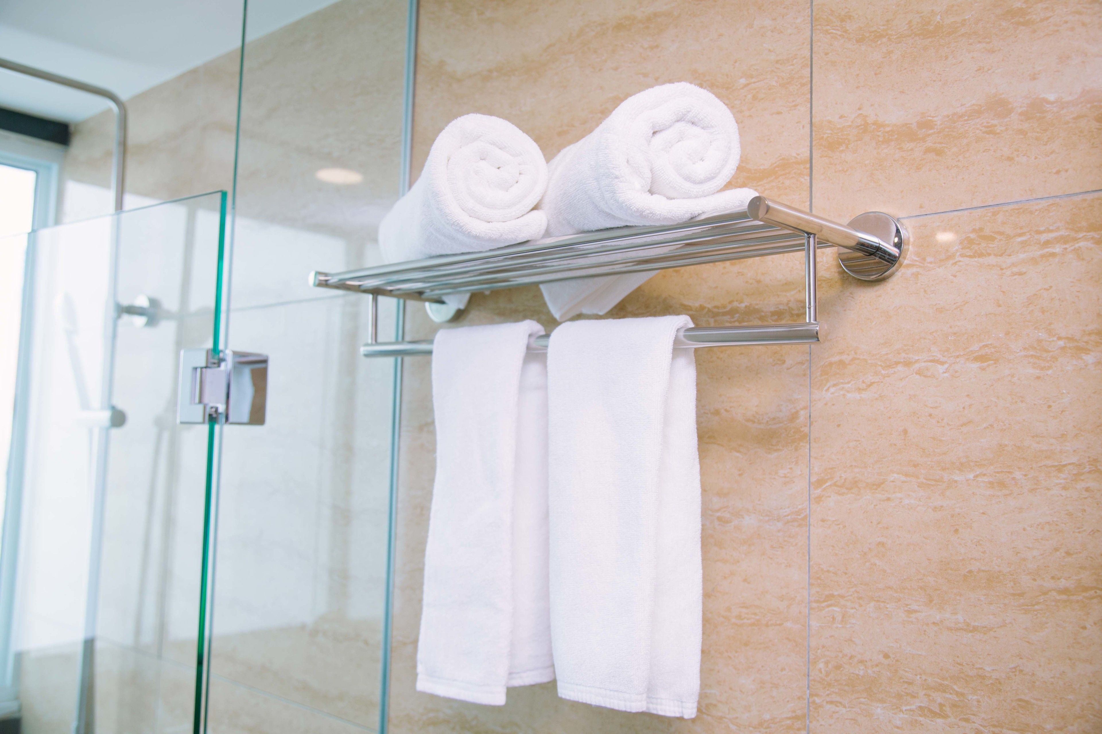 A bathroom with a glass shower enclosure, a towel rack with rolled towels, and a marble wall.