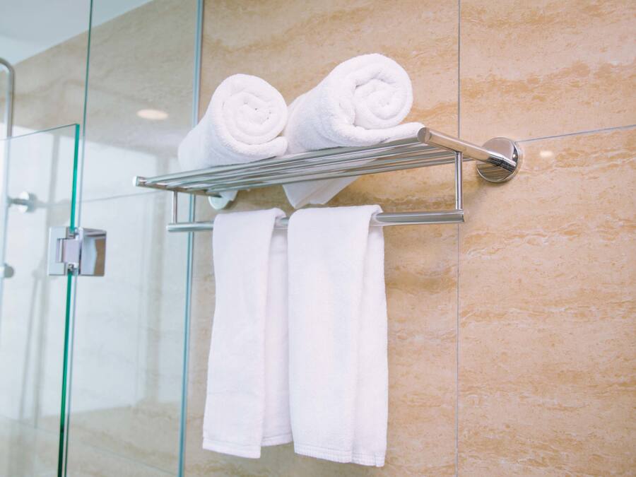 A bathroom with a glass shower enclosure, a towel rack with rolled towels, and a marble wall.
