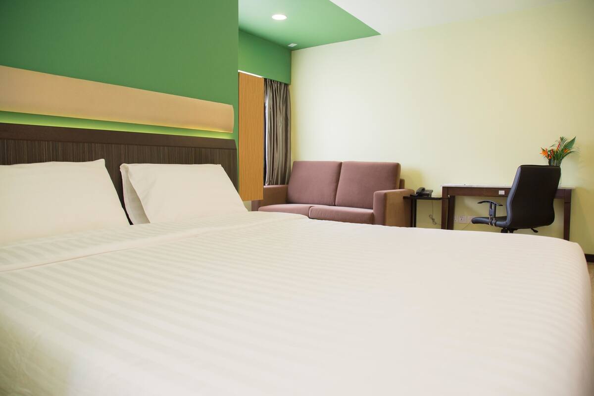 A hotel room with a large bed, a desk, a chair, and a small table with a vase of flowers.