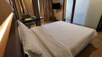 Habitación de hotel con una cama grande, un escritorio con una silla, televisión y una puerta corrediza que da a un baño.