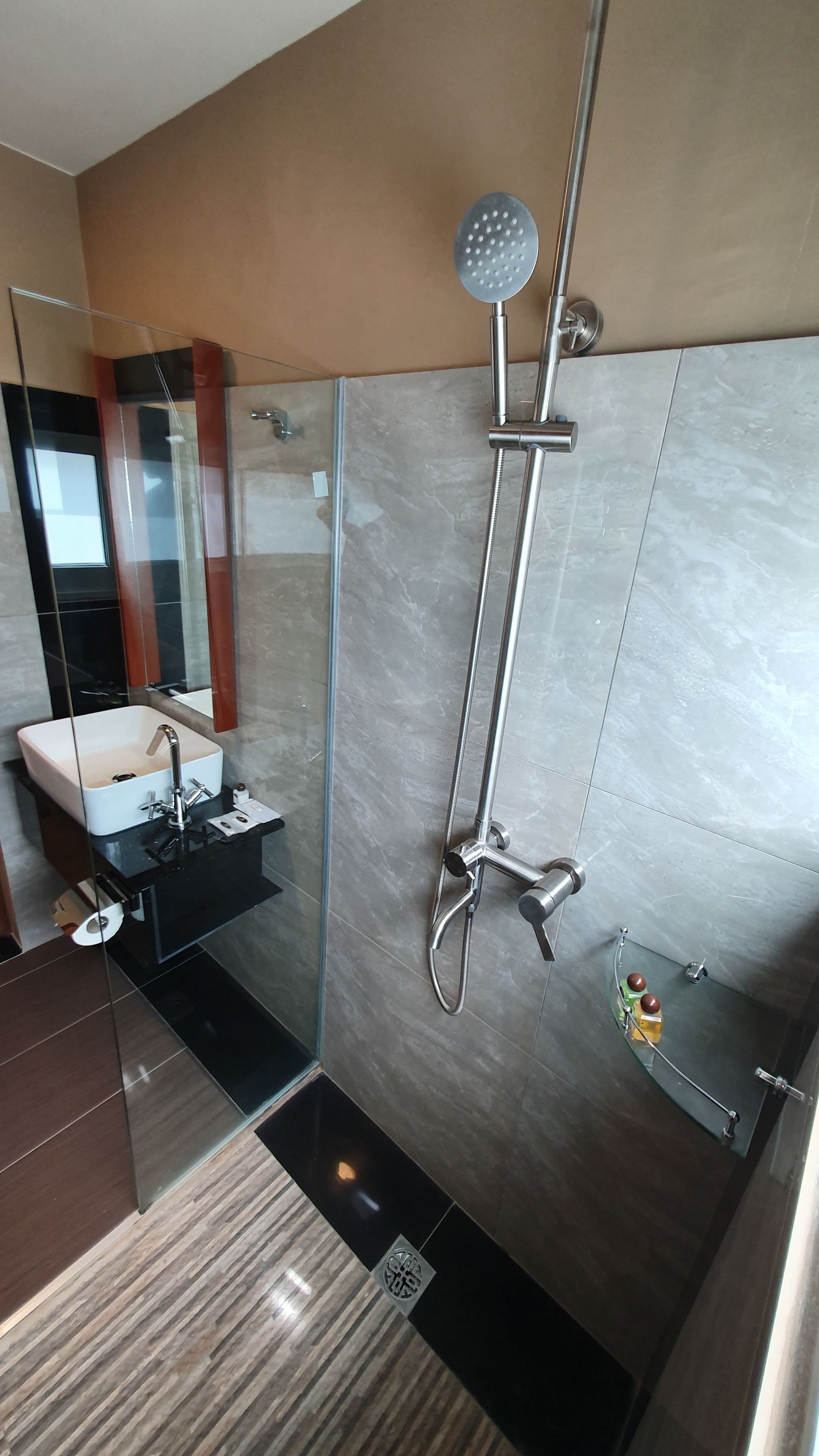 A modern bathroom with a glass-enclosed shower, a sink with a mirror, and a small shelf with toiletries.