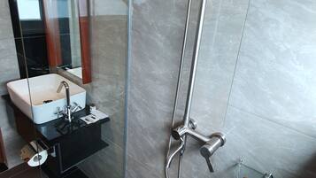 A modern bathroom with a glass-enclosed shower, a sink with a mirror, and a small shelf with toiletries.