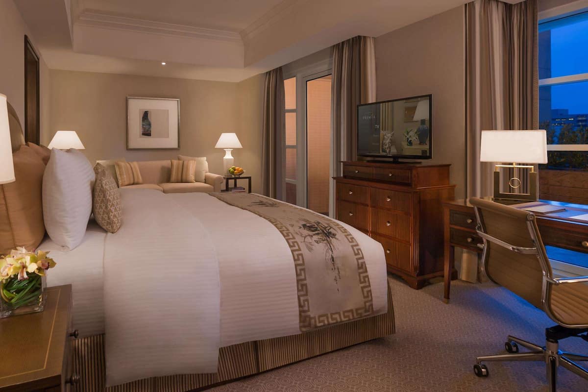Una habitación de hotel con una cama grande, un escritorio con una silla, un televisor y una ventana con cortinas.
