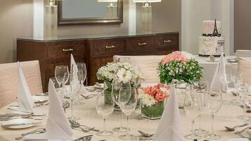 A formal dining table set with white tablecloth, glassware, and silverware, with floral centerpieces and a mirror above.