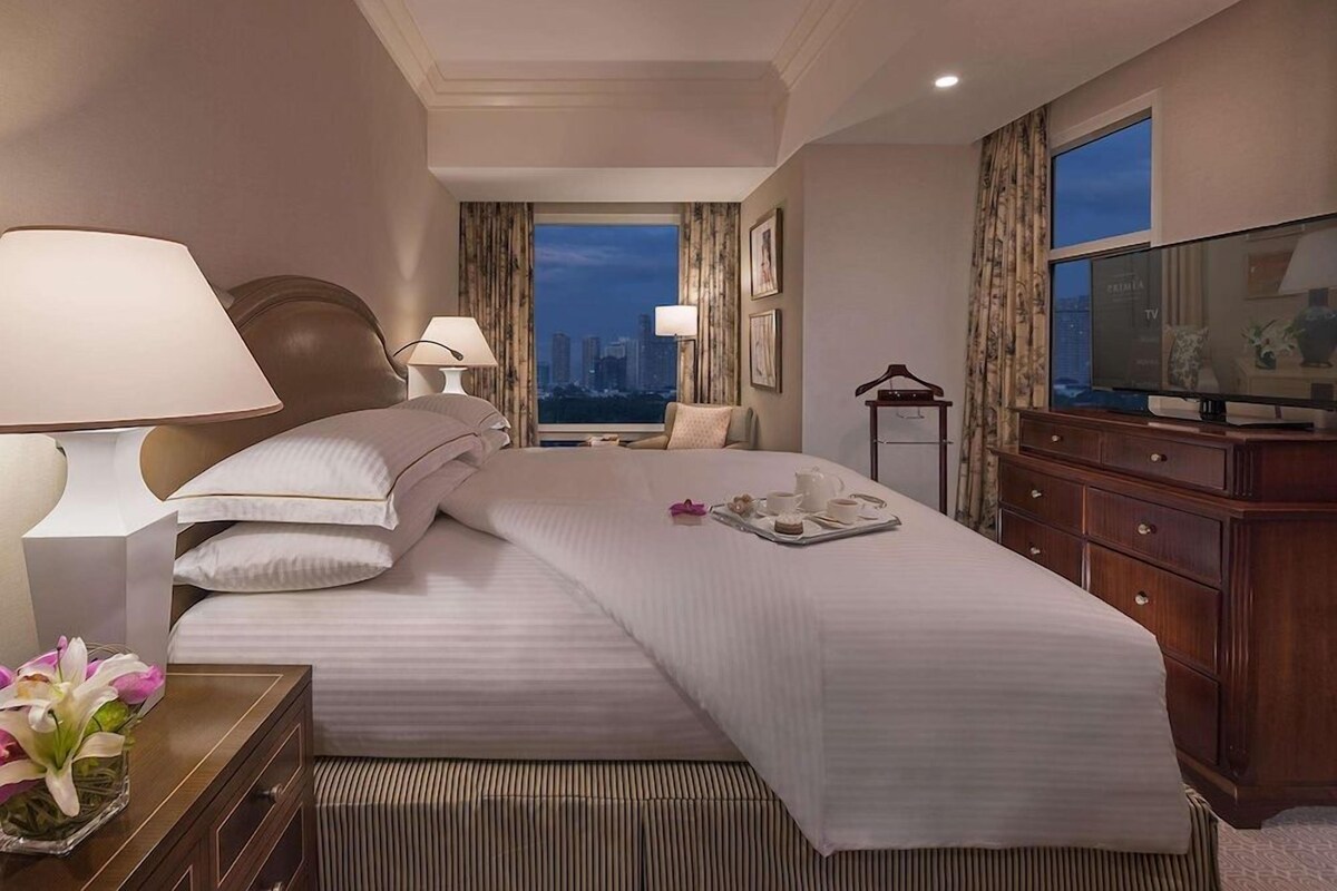 A hotel room with a large bed, a TV, a dresser, and a view of the cityscape.