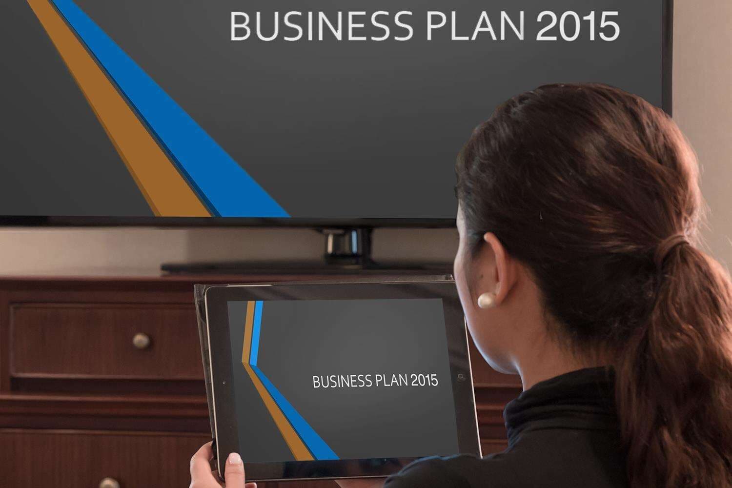 A person holding a tablet displaying 'BUSINESS PLAN 2015' with a TV in the background.