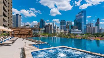 A rooftop pool with lounge chairs and a hot tub, overlooking a city skyline.