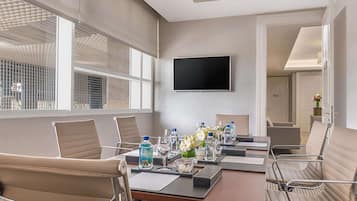 A conference room with a long table, chairs, a flat-screen TV, and a window with blinds.