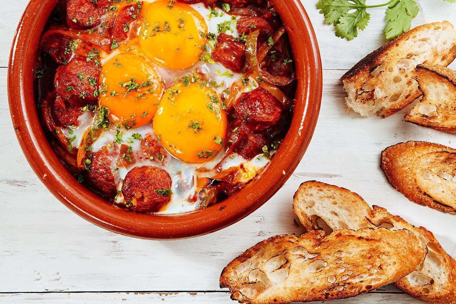 Un plato con huevos, salchicha y pimientos en una olla de barro.