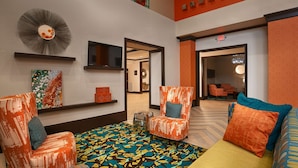 Eine Hotelhalle mit modernem Design, mit einem gemusterten Boden, orange- und blau gemusterten Stühlen und einem großen Spiegel an der Wand.
