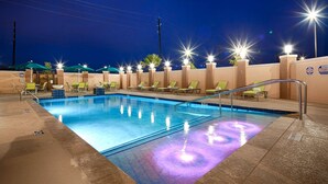 Ein Pool mit Liegestühlen und Sonnenschirmen, umgeben von Mauern und hellen Lichtern.