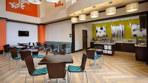 Ein Hotel-Speisesaal mit mehreren Tischen und Stühlen, einer Buffet-Theke und einer Sitzecke mit einer Couch.