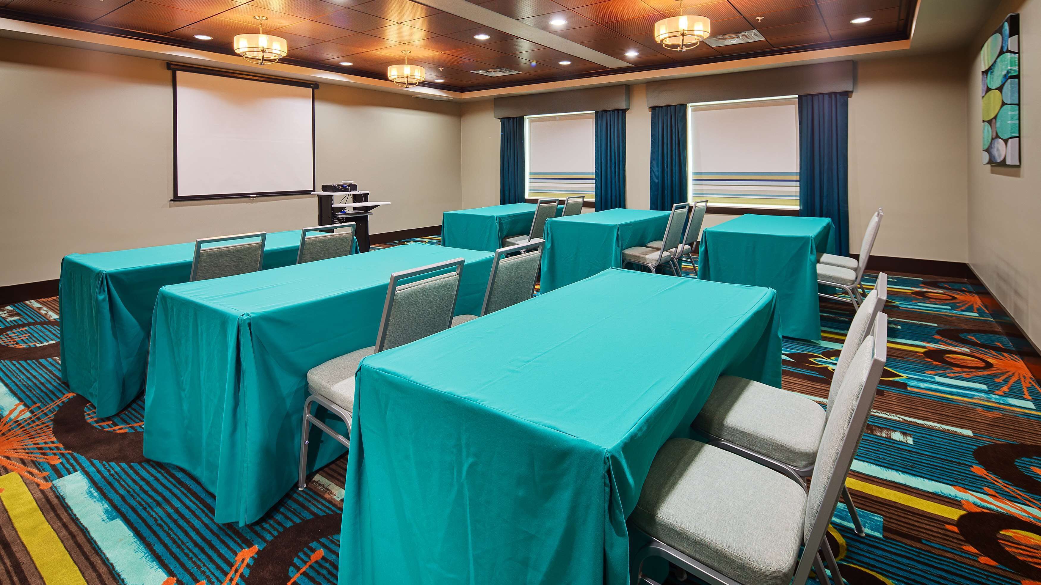 Un salón de conferencias con manteles color aguamarina, sillas grises y una pantalla de proyector.