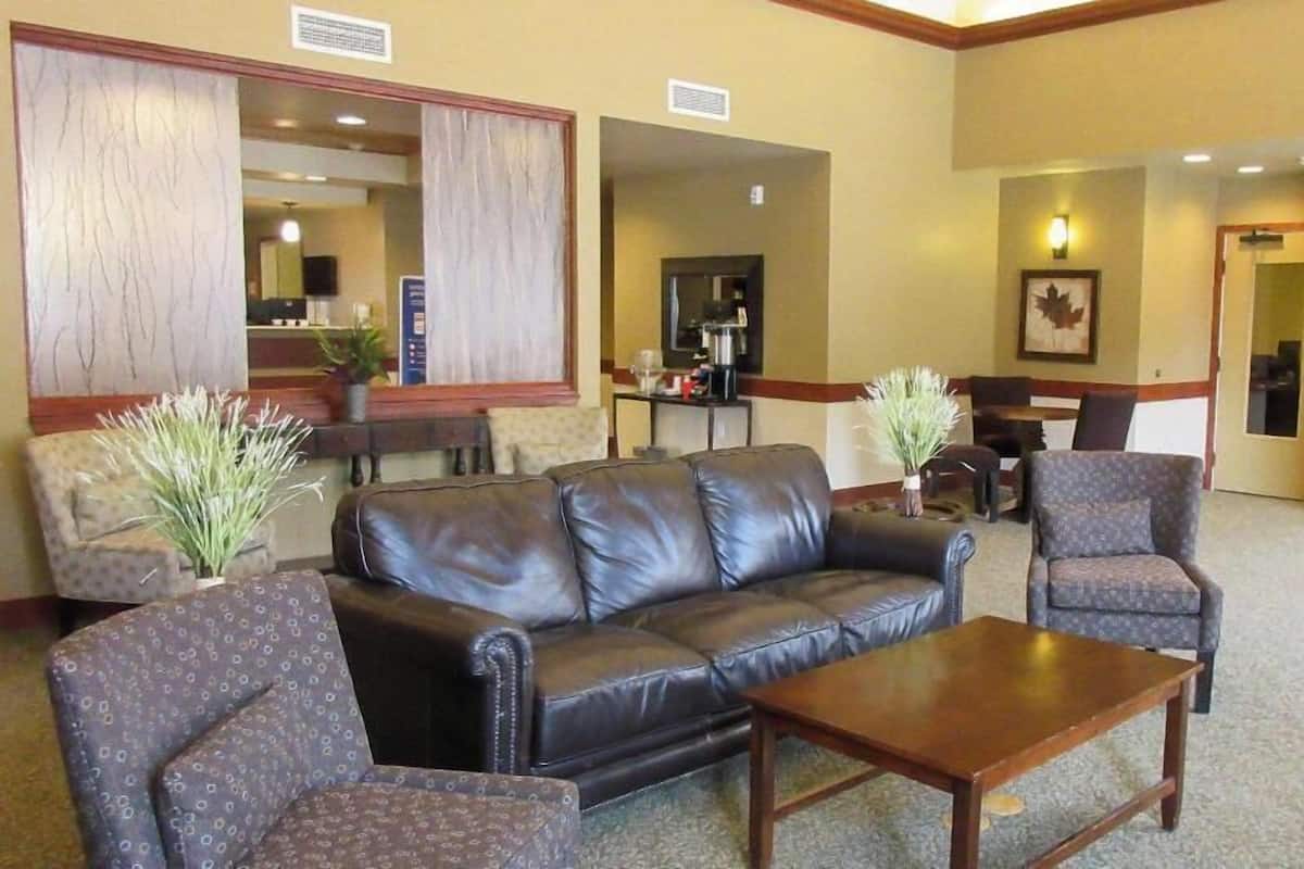 Un hall con un sofá de cuero, sillones estampados, una mesa de centro de madera, un mostrador de recepción y un cuadro enmarcado en la pared.