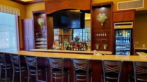 A bar area with a counter, multiple stools, and a refrigerator stocked with beverages. - Clarion Hotel & Suites Williston (Williston)
