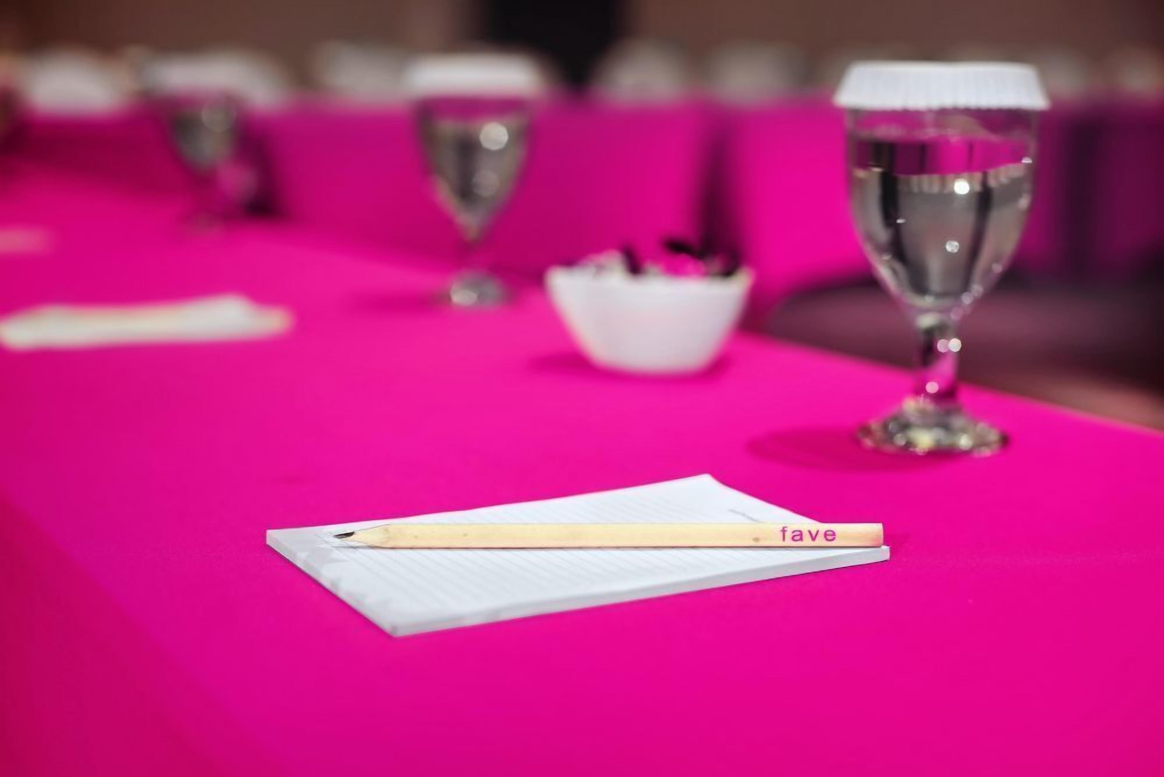 A table with a pink tablecloth, a white notepad, a pen, and a glass of water.
