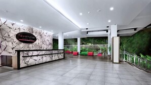 A hotel reception area with a modern design, featuring a reception desk, seating area, and a green wall with a forest view.