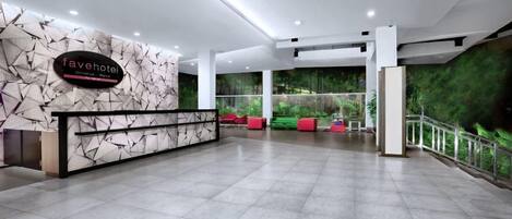 A hotel reception area with a modern design, featuring a reception desk, seating area, and a green wall with a forest view.