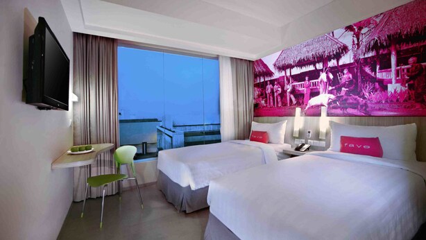 A hotel room with two beds, a desk, a chair, and a large window with a view of a balcony.