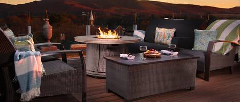 Una terraza con mobiliario de mimbre, una mesa redonda con chimenea y una vista panorámica de colinas al fondo.